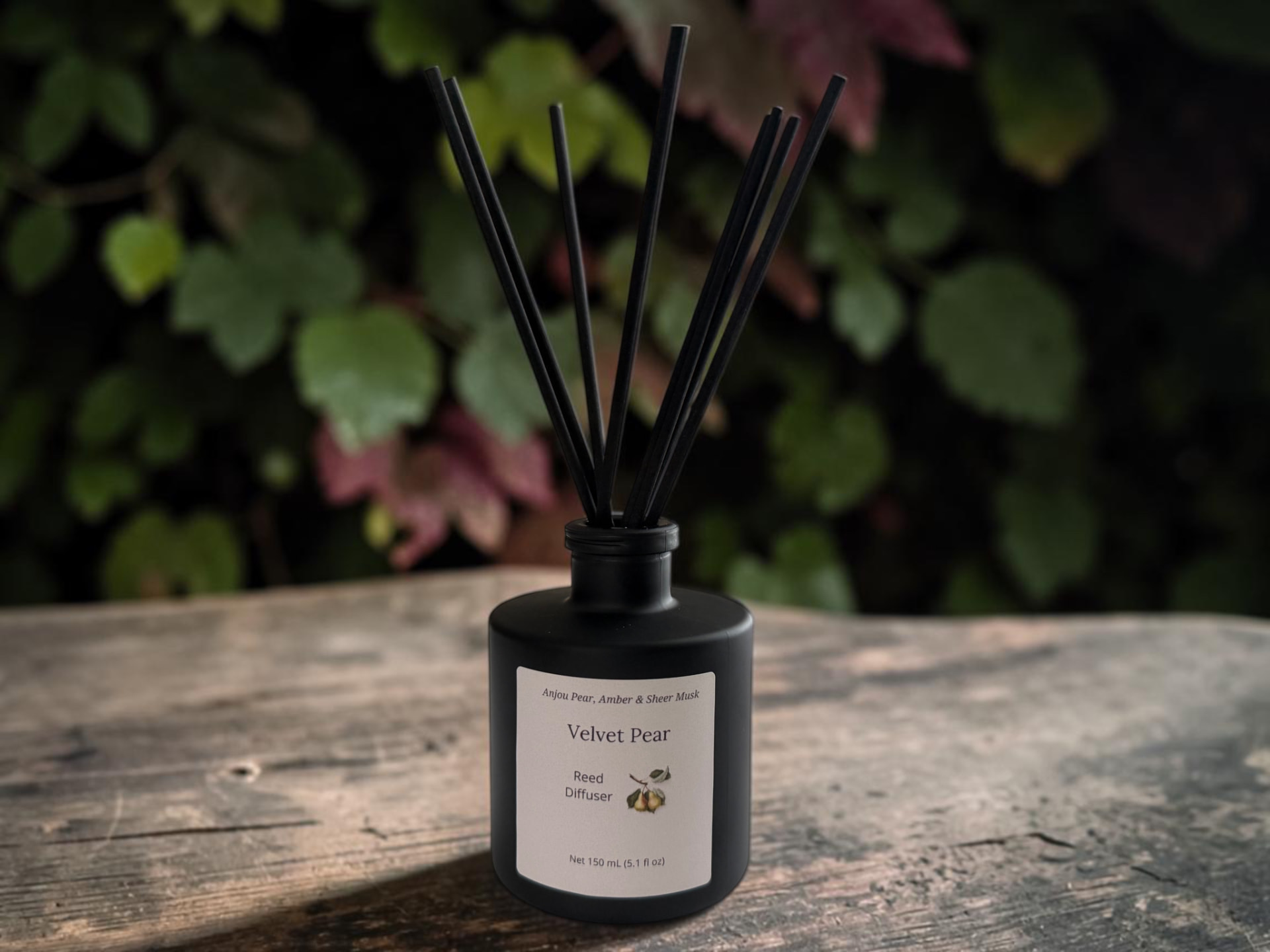 Velvet Pear Reed Diffuser, a matte black bottle with black reeds set against autumn leaves