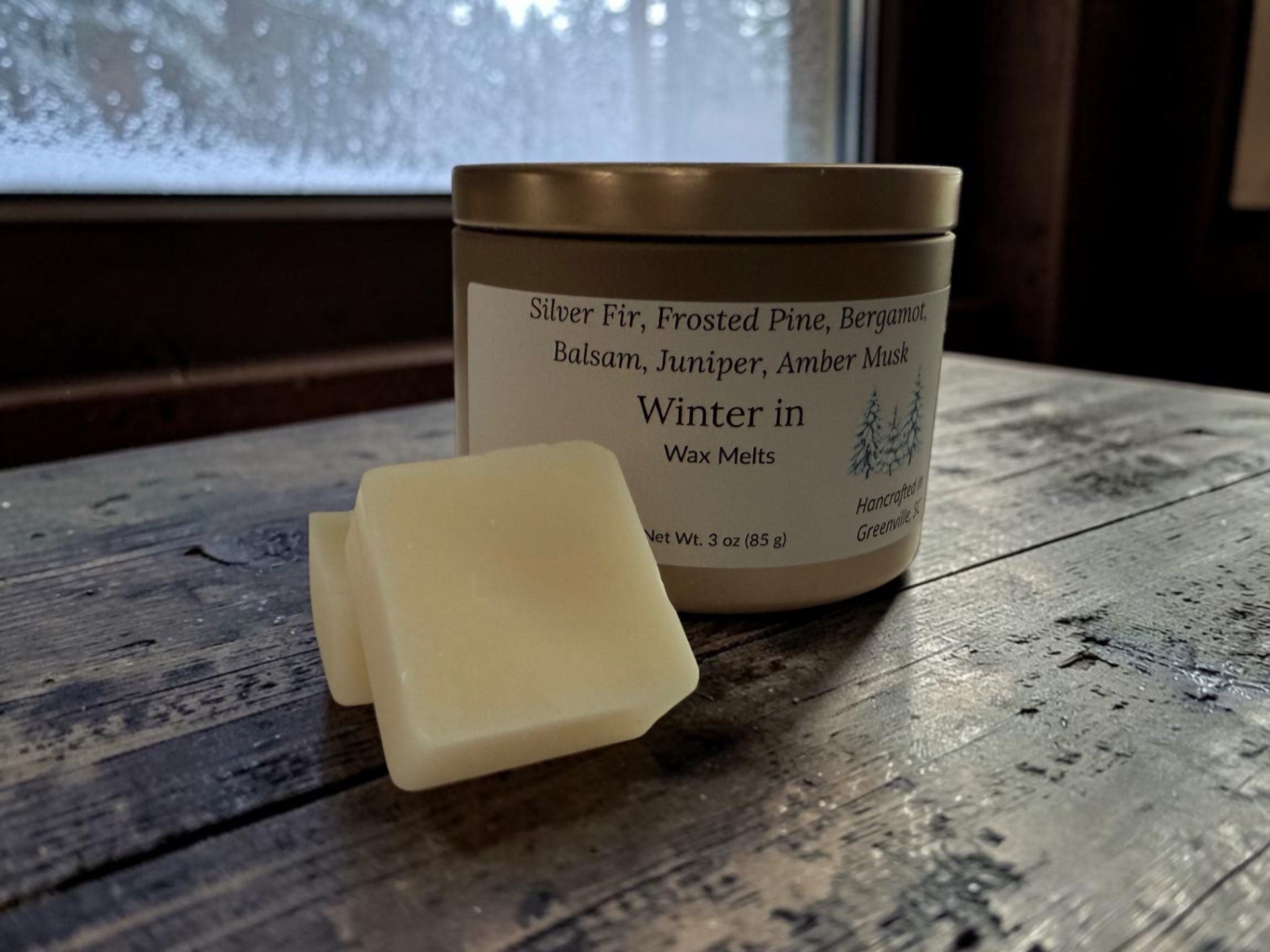 Winter In Wax Melts, a gold tin with creamy wax melt squares on weathered wood in front of a snowy window