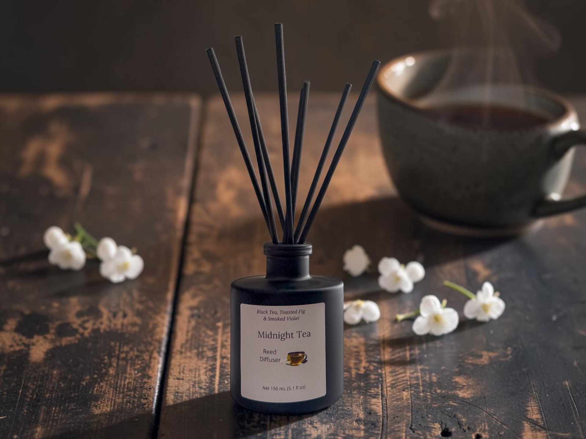 Midnight Tea Reed Diffuser, a matte black bottle with black reeds beside white jasmine blossoms and loose black tea leaves on weathered wood